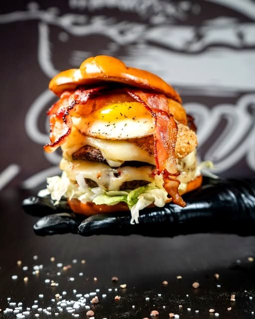 Hoher Burger mit Bacon, Spiegelei und geschmolzenem Käse auf einer dunklen Schieferplatte.