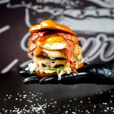 Hoher Burger mit Bacon und Spiegelei auf dunkler Platte.
