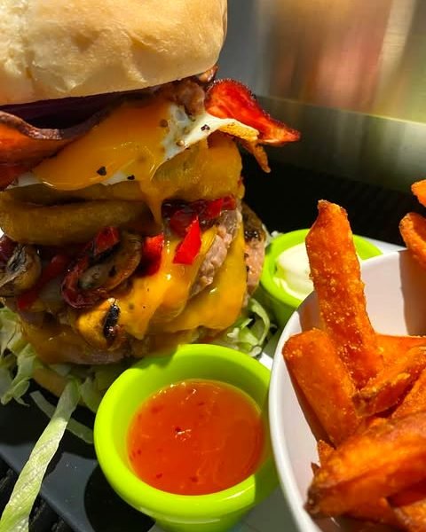Doppelter Cheeseburger mit Süßkartoffel-Pommes und zwei Dip-Schälchen.